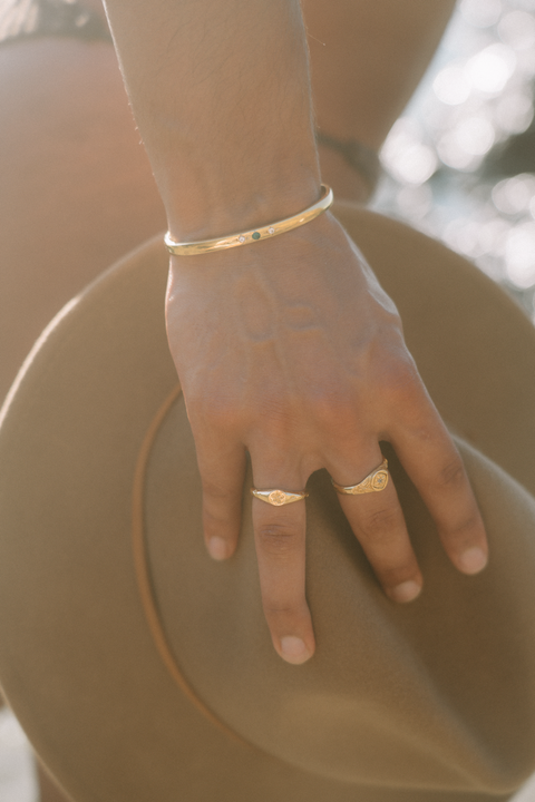 Plumeria ring in 24ct gold plate — worn with a gold signet and gemstone cuff in sunlight