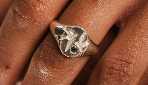 Loyal Signet in sterling silver — close-up worn view of swallows and blue topaz