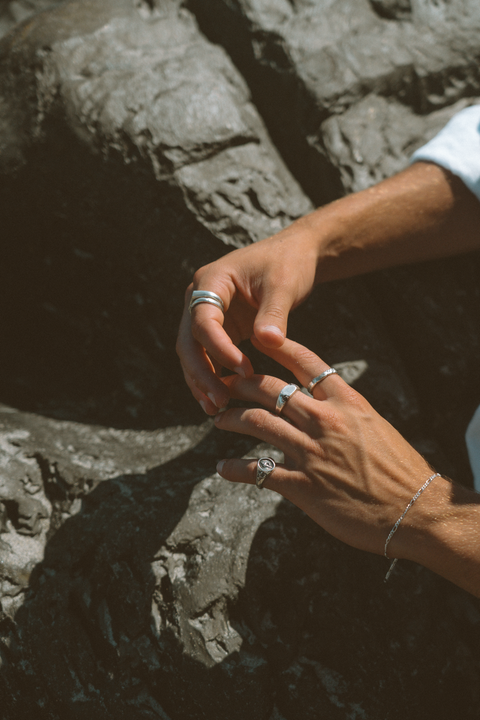 Lou's Stacker in sterling silver — worn with mixed silver rings beside coastal rocks