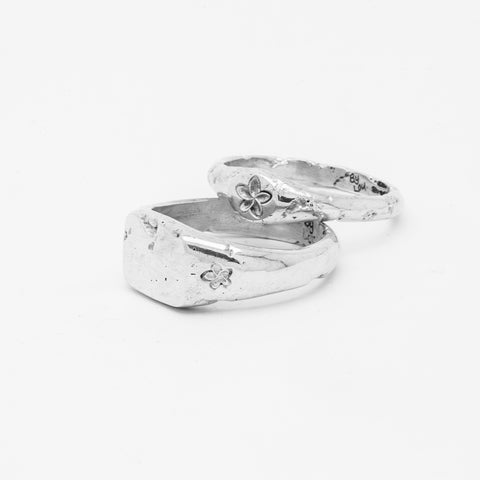 Plumeria ring in sterling silver — displayed behind a wide silver floral signet