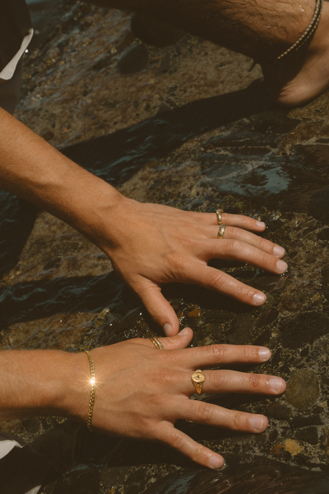 Serene I ring in 24ct gold plate — worn with other gold rings beside a rock pool