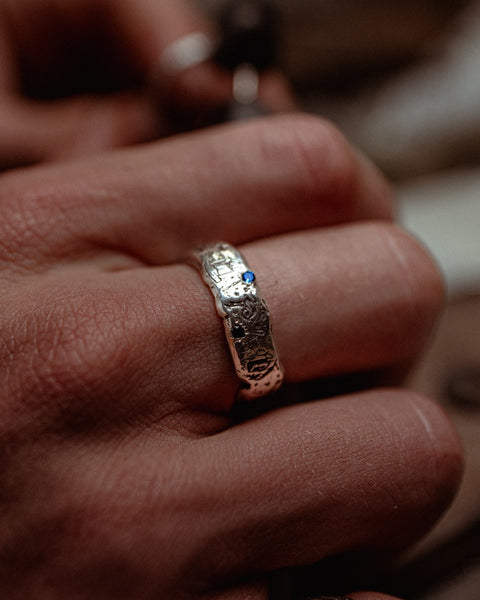 Lou's Grad Ring in sterling silver — close-up worn side view with one blue gemstone visible