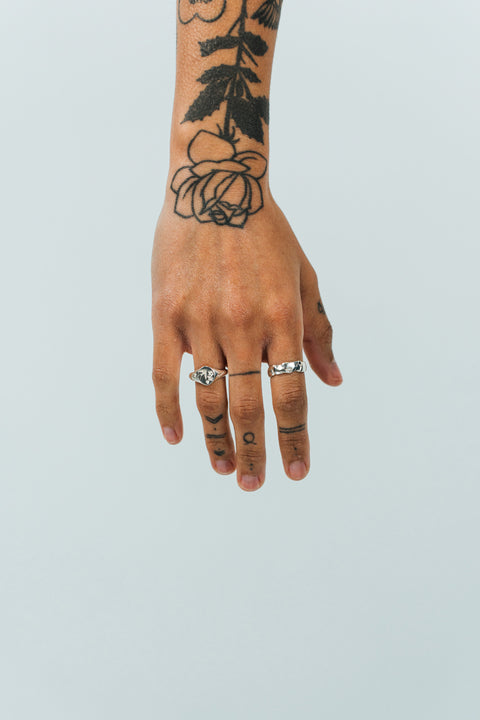 Coalesce ring in sterling silver — worn on a tattooed hand beside a silver signet
