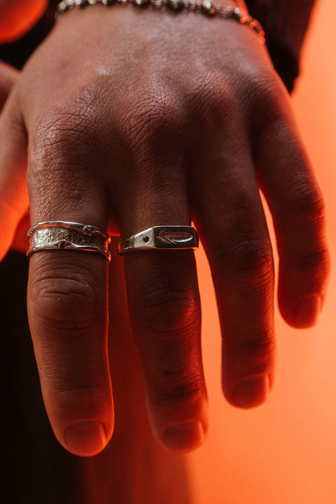 Feather Signet in sterling silver — worn under orange light with the feather face visible