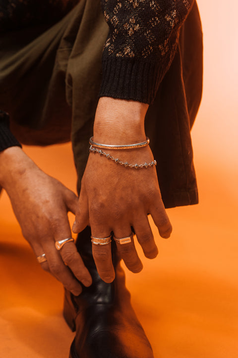 Signature Bracelet in sterling silver — worn below a silver cuff against an orange background